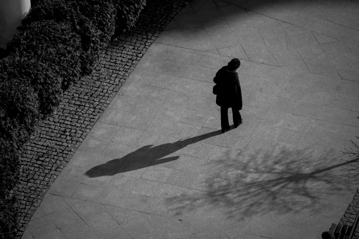 Lone pedestrian casting a long shadow across an open plaza seen from above